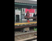 Old man in red flannel cowboy hat holds big red fake fish, then dances and yells in the middle of train station
