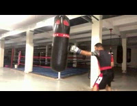 Guy wearing boxing gloves hits punching bag 