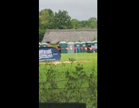 Gray car drags porta potty while guy holds on