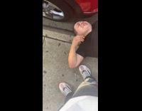 Black shirt guy lays ground red car 