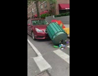 Newspaper boxes and green trash can flipped over on red car 