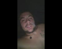 Shirtless guy in bed hits vape pen and blows some smoke at camera 