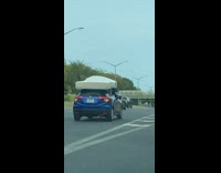 People in blue car hold mattress roof