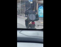 Guy rides motorcycle with a large speaker 