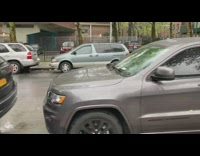 Two parked cars on street both with broken smashed rear windows 
