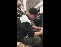 Guy plays drums with drum pad on his lap on the subway