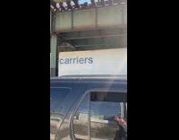 White delivery truck drives under bridge carriers 