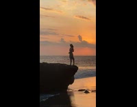 Woman stand edge of rock beach sunset