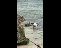Woman poses on beach rock with moss