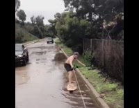 Shirtless guy in black shorts wakeboarding on flooded streets falls immediately