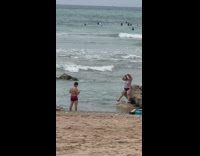 Woman in striped bikini poses on beach rock 