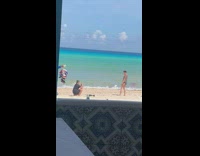 Shirtless guy poses on shore near guy with bunch of hats 