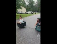 Two girls in black and green cart race down street 