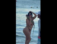 Collab IITW - Woman in bikini and sunglasses poses with an iguana with sombrero at the beach