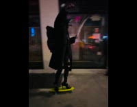 Collab WINY - Man in black  rides skateboard on heels at sidewalk