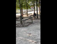 Woman goth outfit poses beside tree fence