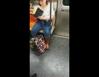 Woman reading book on subway train has holes in pants on her crotch area 