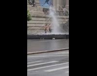Group of people run through water fountain in front of museum 