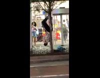 Guy hangs upside down from tree and plays the flute in front of store