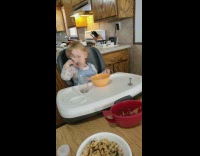 Baby eats food with eyes close in the table