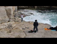 Guy dances on brown rock by water