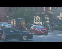 Red shirt guy rides bicycle with ball on head 