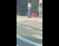 A woman has a small red dog on corner of street