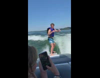 Guy surfs on wave created by boat on lake 