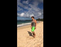 Guy jumps on yellow yoga ball at the beach and pops it