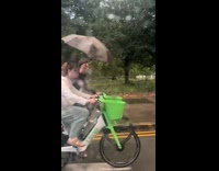 Couple ride bike together man holds umbrella