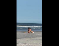 Woman in brown bikini kneels at the beach blanket