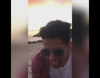 Guy in red shirt talks with alien voiceover at beach sunset