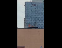 Shirtless guy swings two sticks around on roof 