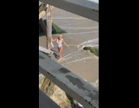 Blonde lady in white swimsuit poses below pier 