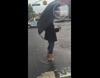 Woman with green make up black umbrella plays in rain puddle with bare feet on the street and sings