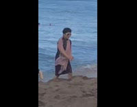 Woman in a black dress and a scarf poses at the beach