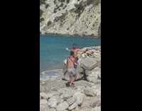 Man shirtless blue shorts flex muscle on a beach rock