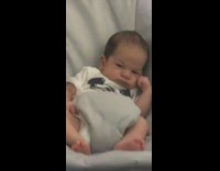 Infant baby with straight face and hand on cheek looks annoyed and mad inside electric rocking seat chair