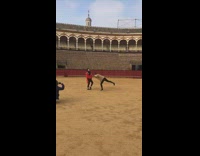 Girl points fingers on head like a bull and poses with friend with red bullfighter flag