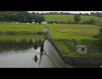 Guy slides down the side of steep river dam on bodyboard