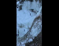 Tourists take photo by partially frozen waterfall 