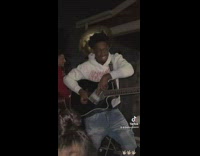 Guy playing black guitar with clear bottle of alcohol