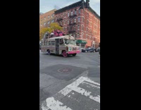 Rainbow and pink bus with people on top of it 