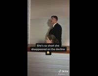 Short woman in dress disappears behind ledge