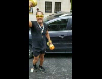 Guy standing outside car holds yellow dumbbells and practices punching