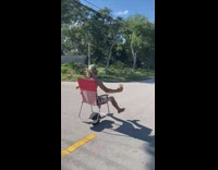 Guy rides one wheel with red lawn chair on road 