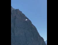 Guy jumps grey mountain white parachute windy