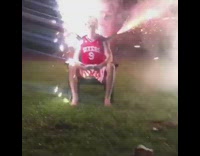 Guy in red sixers jersey sits in exploding  fireworks chair 