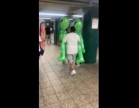 Guy walking carries two alien inflatable balloons
