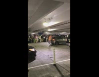 Shirtless guy plaid shirt around waist walks around underground parking lot in the middle of traffic